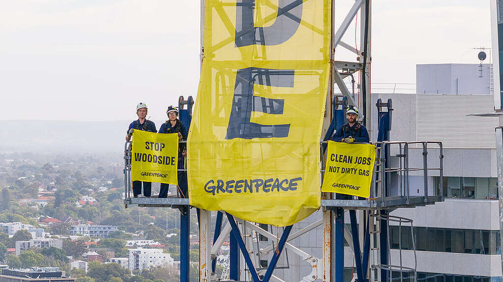 Greenpeace Australia activists hold banners from a crane outside Woodside's headquarters in Perth. 
