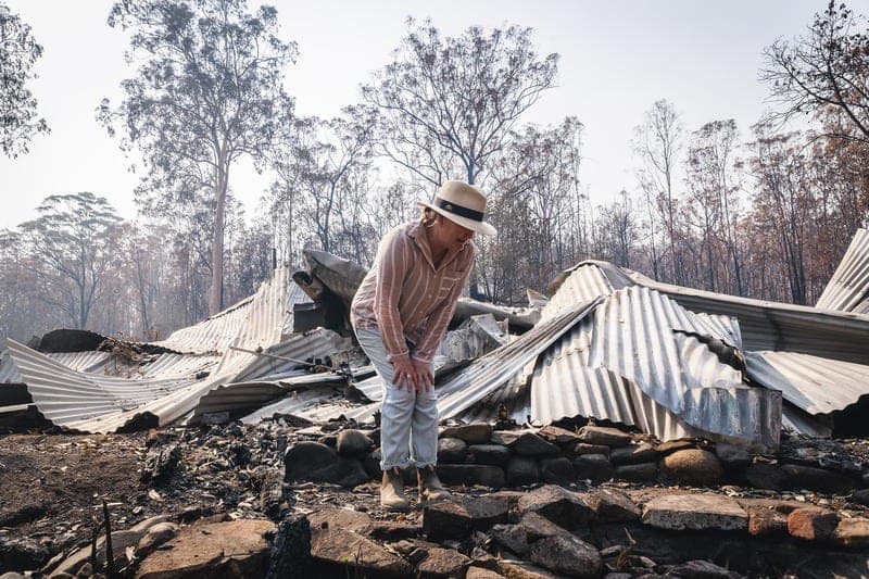 Bushfire survivor Melinda Plesman examines the remains of her destroyed property in Nymboida, NSW. Corrugated iron sheets lay warped and ruined in the background, completely destroyed by the heat of the fire. 