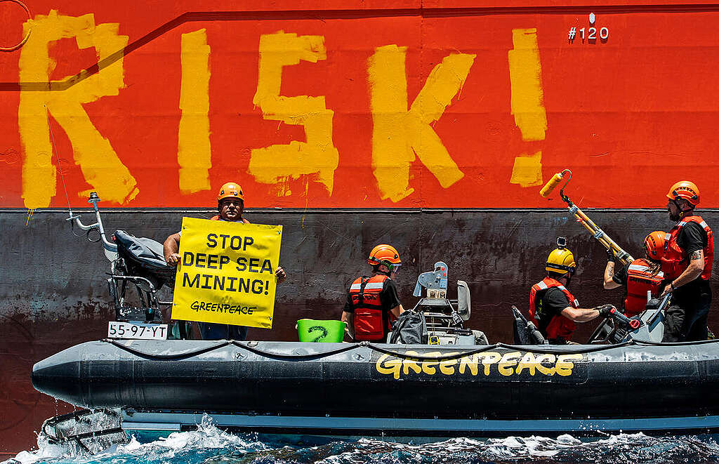 Greenpeace International activists paint the word 'RISK!' on the starboard side of Normand Energy, a vessel chartered by the Belgian company Global Sea Mineral Resources (GSR) to commercially extract minerals from the seabed in the future.  The Greenpeace ship is in the Clarion Clipperton Zone in the Pacific to bear witness to the deep sea mining industry.